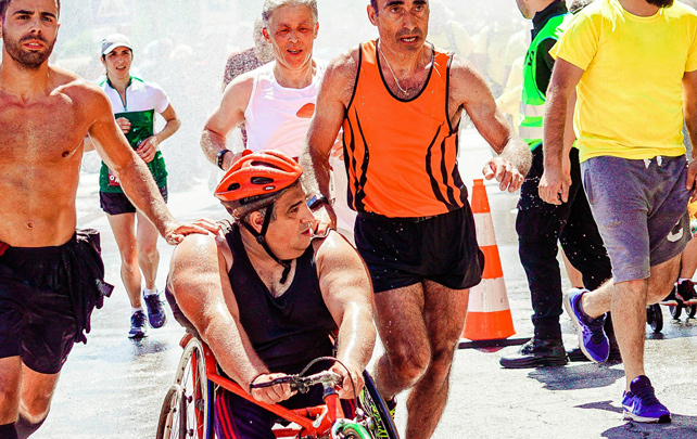 A gentleman in a wheelchair with a boy and a gentleman running alongside him