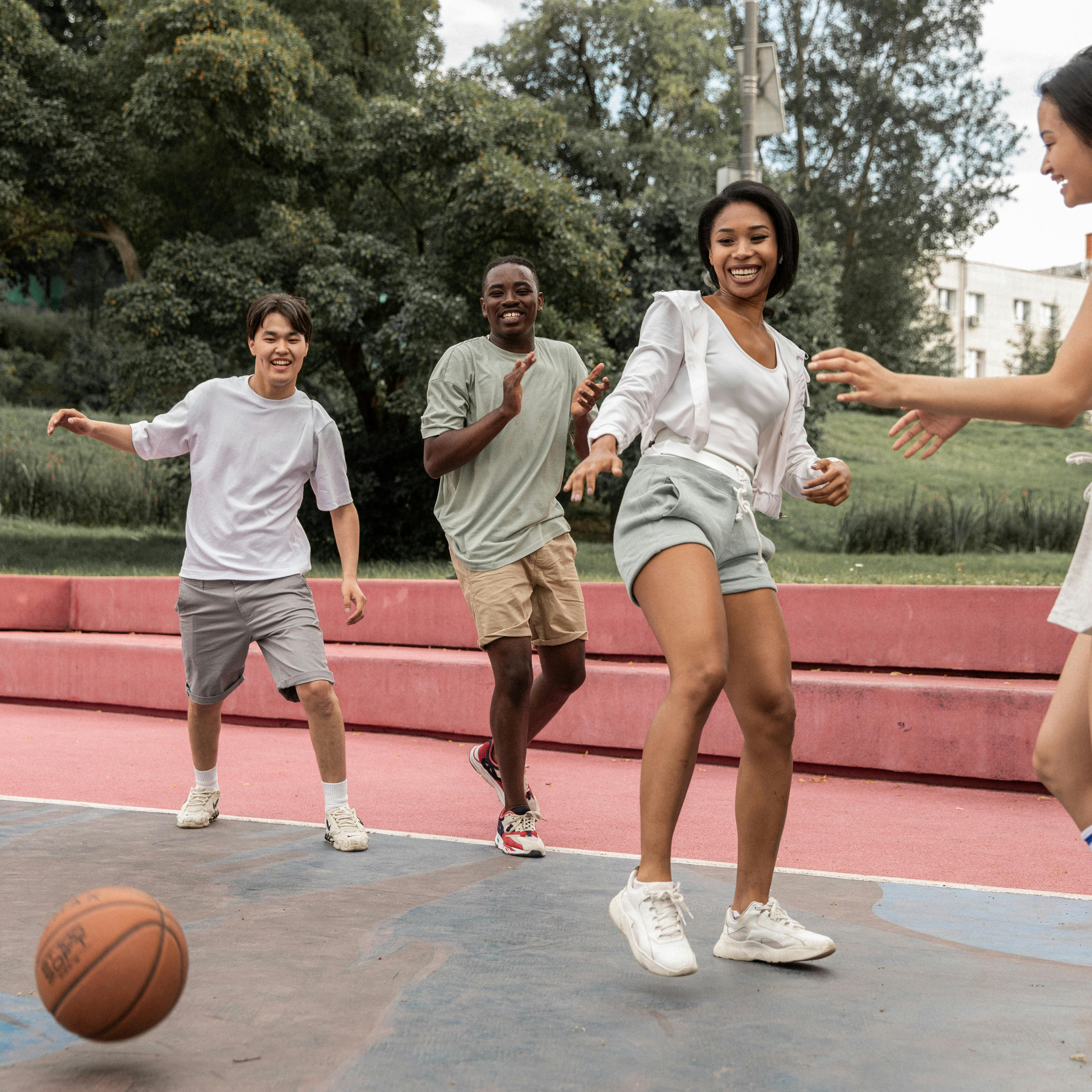 two girls and two boys playing basketball on an outdoor court