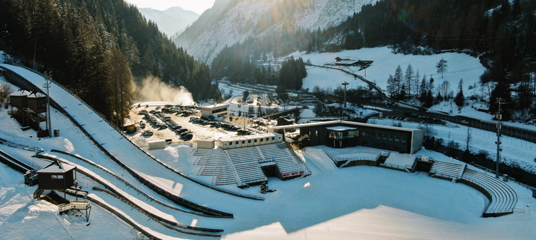 The sun shines through the mountains above the Predazzo Ski Jumping Stadium​ track