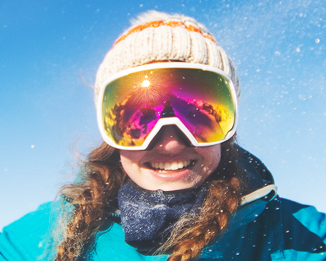 Immagine di una ragazza sorridente con maschera da sci e cappello