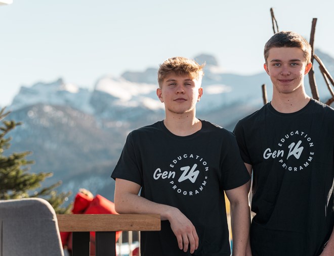 Due giovani indossano magliette nere con il logo di Gen26, sullo sfondo le montagne
