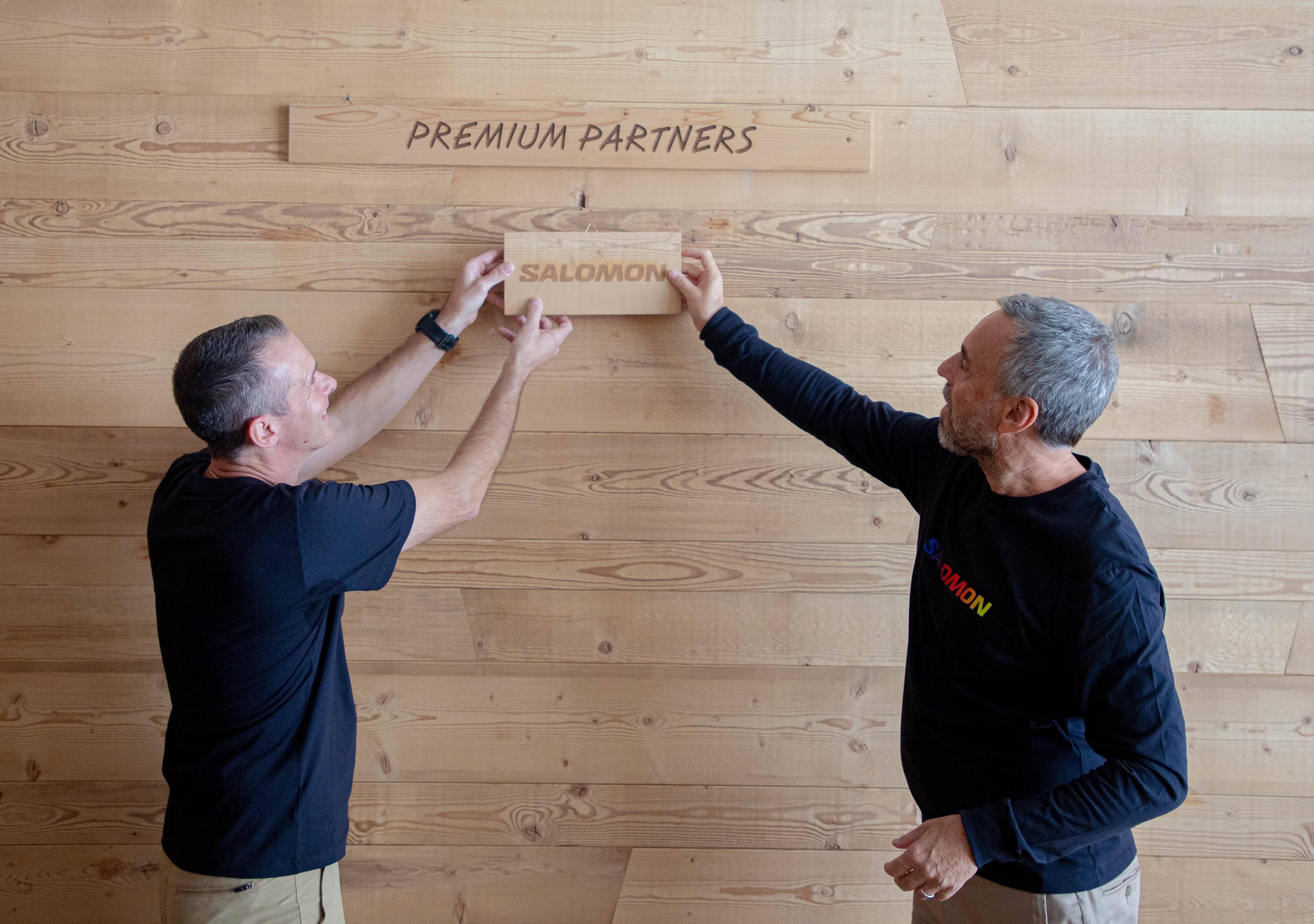 Foto di Varnier e Franco Fogliato mentre applicano la targhetta  'Salomon' nel muro delle partnership