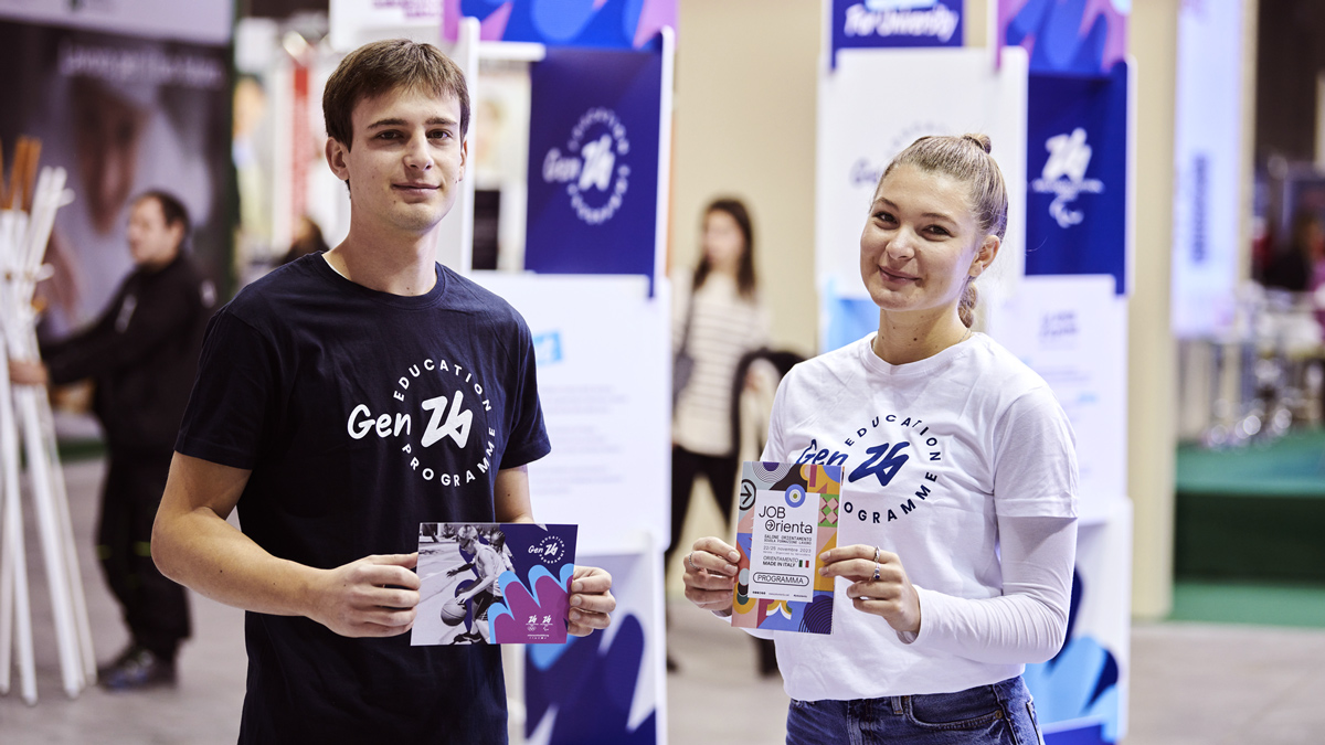 A boy and a girl wearing Gen26 shirts holding flyers of the Gen26 dual career- Job oriented event