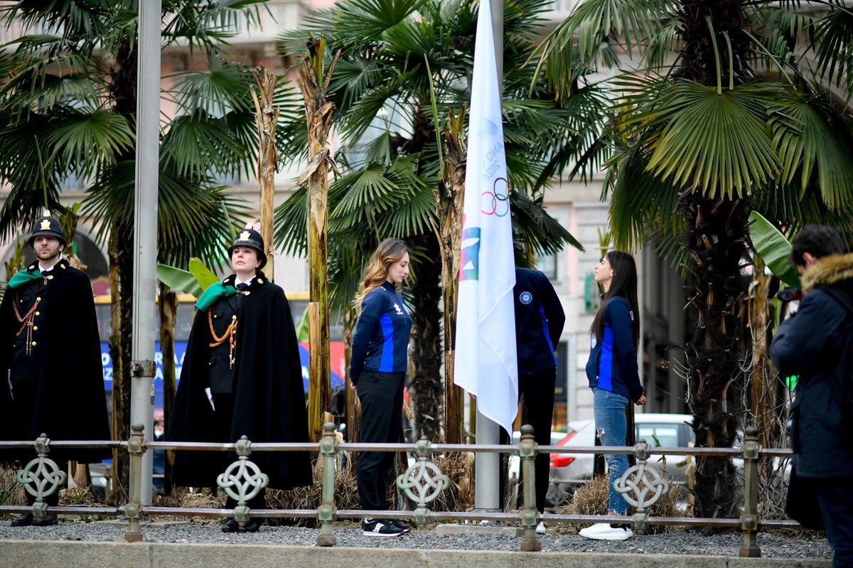 Due ragazze in piazza Duomo di Milano davanti alla bandiera Olimpica e Paralimpica di Milano Cortina2026