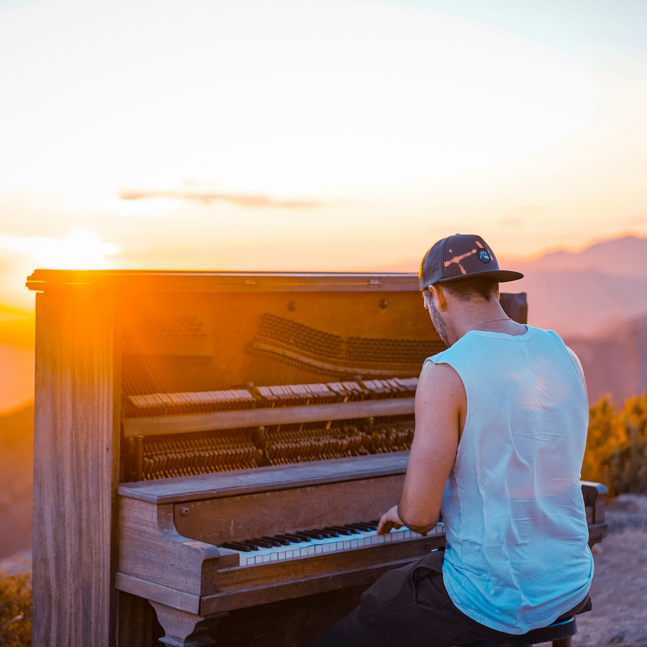 Un ragazzo con il cappellino che sta suonando il pianoforte al tramonto in un paesaggio collinare