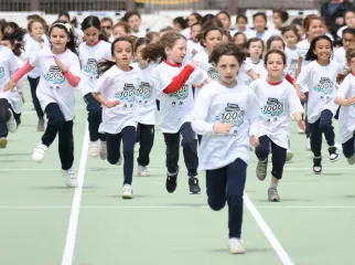 Dei bambini che corrono su un campo di atletica con la maglia di Milano Cortina 2026